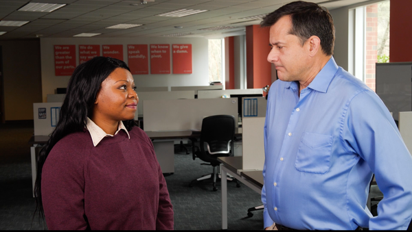 A Black woman and a White man having a conversation in an office