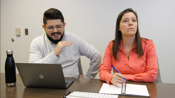 A Latine man and a White woman sitting next to each other at a desk